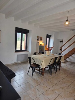 A dining area with a table set for four, a staircase, and a window with a view. - Vrbo Property (Terre-et-Marais)