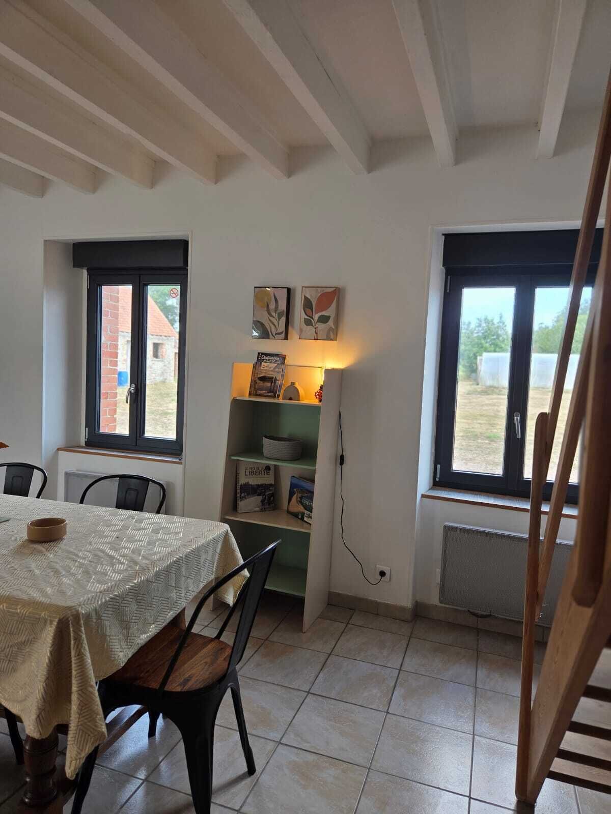Ein Essbereich mit einem Tisch für zwei Personen, einem Bücherregal mit Büchern und Dekorationsobjekten sowie einem Fenster mit Blick nach draußen.