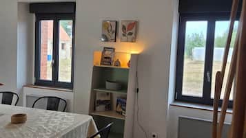 Ein Essbereich mit einem Tisch für zwei Personen, einem Bücherregal mit Büchern und Dekorationsobjekten sowie einem Fenster mit Blick nach draußen.