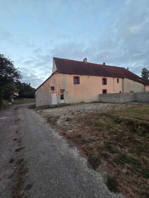 A two-story building with a red-tiled roof, a gravel driveway, and a grassy area in front. - Vrbo Property (Terre-et-Marais)