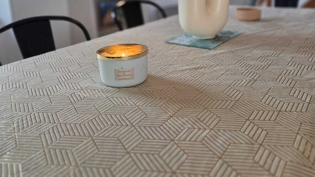 Una mesa de comedor con mantel de estampado geométrico, una vela y un florero con hojas otoñales.