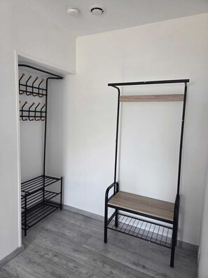 A room with a metal storage unit with shelves and hooks, a wooden bench, and a grey wooden floor.