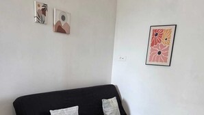 A black sofa with two pillows, a tiled floor, and two framed artworks on the wall.