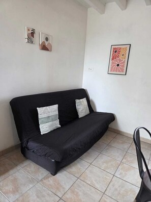 A black sofa with two pillows, a tiled floor, and two framed artworks on the wall.