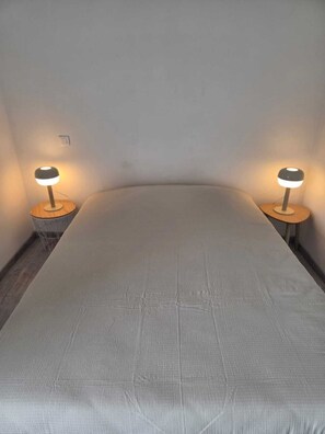 A bedroom with a single bed, two bedside tables, and two wall-mounted lamps. - Vrbo Property (Terre-et-Marais)