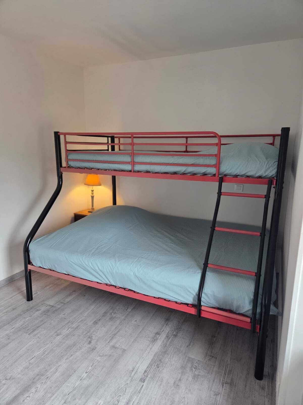 Un lit superposé avec un matelas simple et un oreiller, une table de chevet avec une lampe et un plancher en bois.