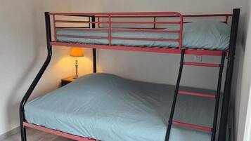 Un lit superposé avec un matelas simple et un oreiller, une table de chevet avec une lampe et un plancher en bois.