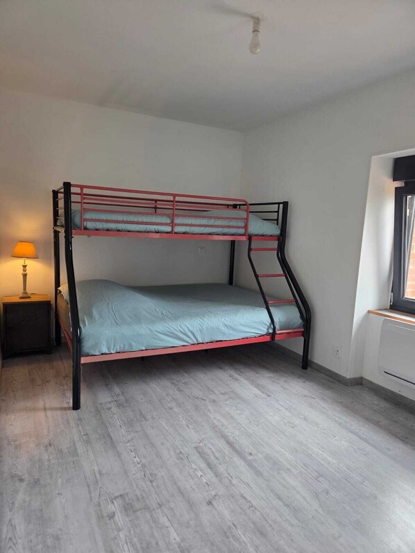 A bunk bed with a single mattress, a bedside table with a lamp, and a window with blinds.
