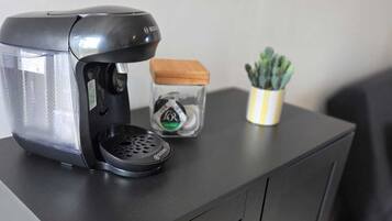 A black coffee maker on a cabinet with a small plant and a container.