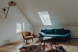 A room with a sloped ceiling, a sofa, a chair, a table, a potted plant, and a window. - Holiday home in Aach with swimming pool (Aach)