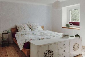 A bedroom with a wooden bed, a white dresser with decorative panels, a bedside lamp, and a window with a view of trees. - Holiday home in Aach with swimming pool (Aach)