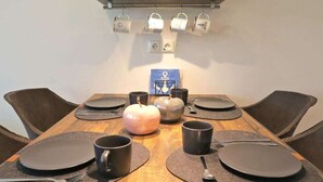 Et spisebord dækket med tallerkener, bestik og krus, med en dekorativ æbleopsætning i midten.