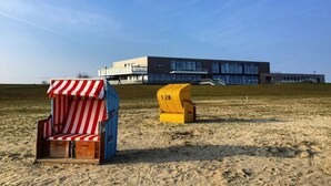 En strand med to liggestole og en moderne bygning i baggrunden.