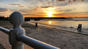 Solnedgang over en strand med gelænder i forgrunden.