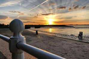 Een zonsondergang boven een strand, met een metalen hek op de voorgrond.