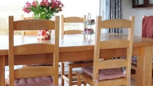A dining area with a wooden table and chairs, a vase with flowers, and a bookshelf in the background. - Charming cottage on Mount Brandon,stunning unimpeded ocean views close to Dingle (Dingle)