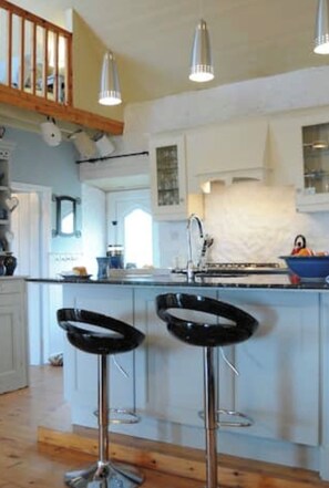 A kitchen with a central island, two bar stools, pendant lighting, and a wooden ceiling.