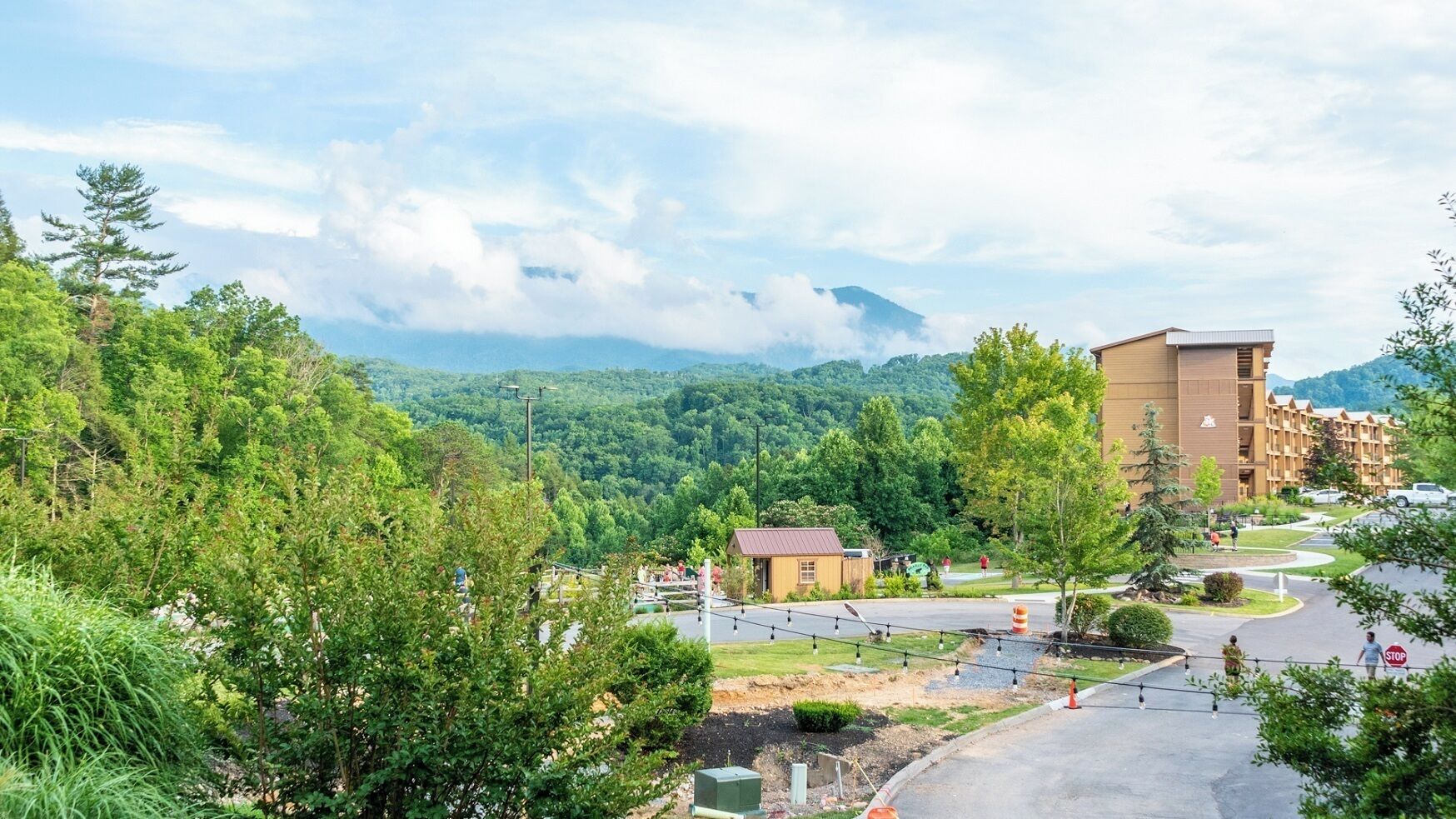 Un hotel con vistas a un paisaje montañoso, un estacionamiento y un edificio pequeño al frente.