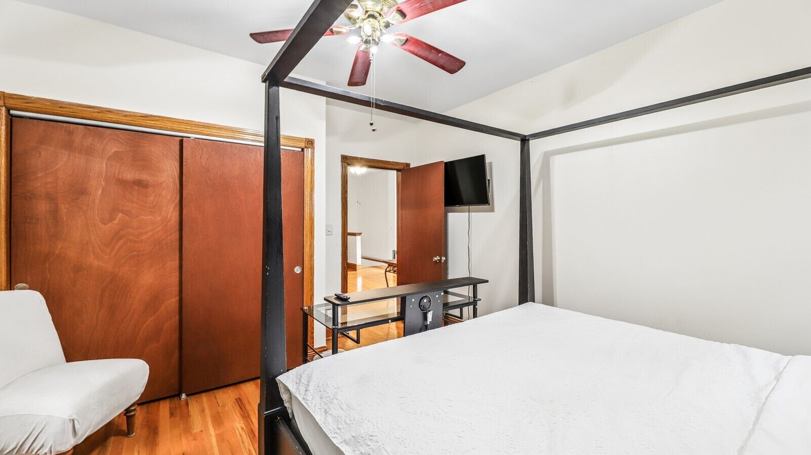 A bedroom with a bed, a desk, a chair, a wardrobe, and a ceiling fan.