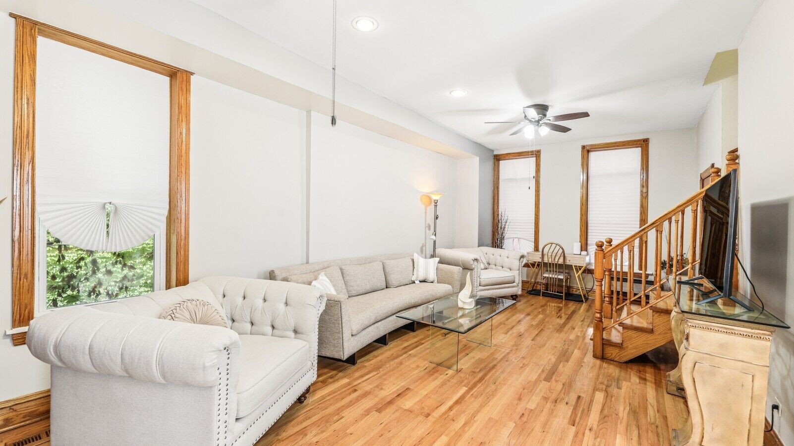 A spacious living room with a large sectional sofa, a glass coffee table, and a wooden staircase.