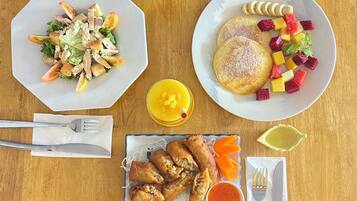 Una mesa de madera con varios platos, incluyendo una ensalada, panqueques con fruta, rollitos primavera fritos y un tazón pequeño de salsa.