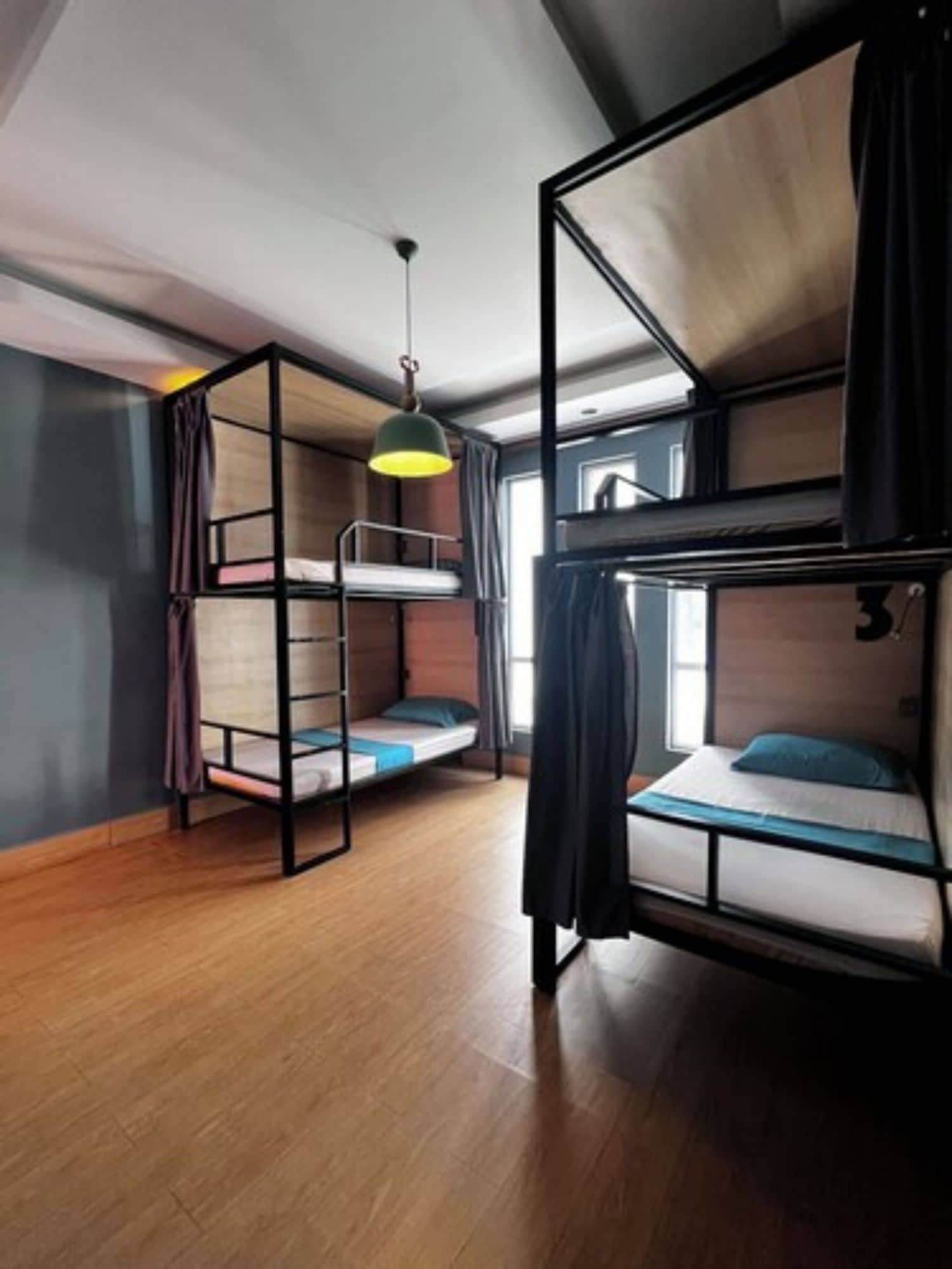 A dormitory room with bunk beds, a hanging light fixture, and a window with curtains.