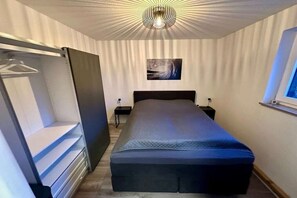 Een slaapkamer met een bed, een kledingkast, een nachtkastje, een aan de muur hangend schilderij en een raam.