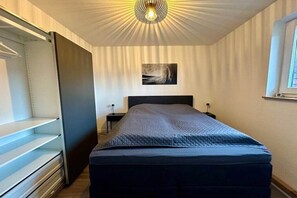 A bedroom with a bed, a nightstand, a wall-mounted lamp, and a ceiling light fixture. - LEEV Wo 12, Schillig Hörn. 2, Schillig (Schillig)