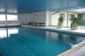 Une piscine intérieure à l’eau claire, avec des bancs le long des bords et des plantes en pot.