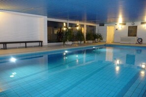 An indoor swimming pool with clear blue water, surrounded by white walls and potted plants. - Holiday apartment in Berchtesgaden with Wi-Fi (Berchtesgaden)