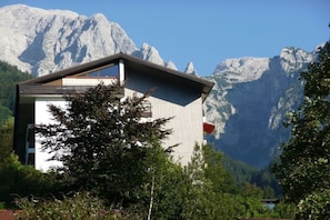 A mountain cabin with a sloped roof, surrounded by lush greenery and a backdrop of rugged mountains. - Holiday apartment in Berchtesgaden with Wi-Fi (Berchtesgaden)