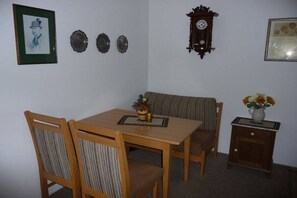 A dining area with a wooden table and chairs, a clock on the wall, and a small cabinet with a vase of flowers. - Holiday apartment in Berchtesgaden with Wi-Fi (Berchtesgaden)