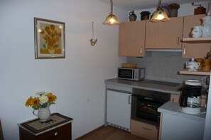 A compact kitchen with a microwave, oven, and coffee maker. There is a small table with a vase of flowers. - Holiday apartment in Berchtesgaden with Wi-Fi (Berchtesgaden)