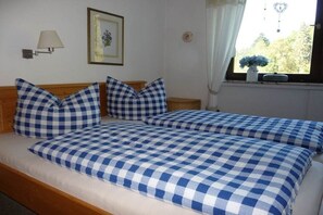 A double bed with checkered bedding, a bedside table, a lamp, a framed picture on the wall, and a window with a view of trees. - Holiday apartment in Berchtesgaden with Wi-Fi (Berchtesgaden)