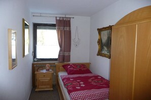 Une petite chambre à coucher avec un lit simple, une armoire en bois, une table de chevet, une fenêtre avec des rideaux et un tableau accroché au mur.
