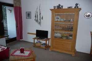 Un salon avec un téléviseur posé sur un meuble, un buffet en bois contenant de la vaisselle et un rideau rouge.