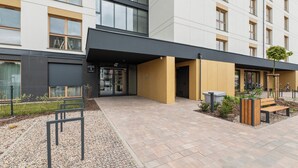 Un edificio moderno con un acceso cubierto, mesas al aire libre y un camino de grava.