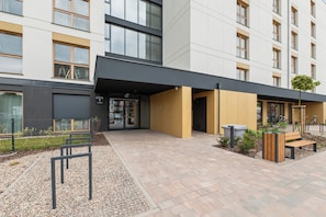 A modern building with a covered entrance, outdoor seating, and a gravel pathway. - Porto Regatta with Parking and Gym (Gdańsk)