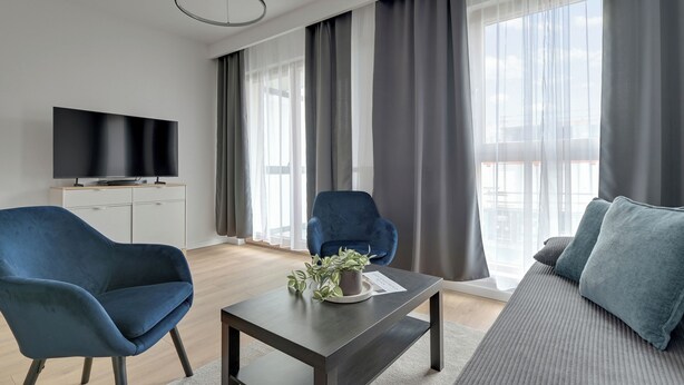 Una sala de estar moderna con un televisor de pantalla plana, dos sillones azules, una mesa baja oscura y un sofá gris.