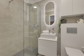 A modern bathroom with a glass shower enclosure, a white sink, and a mirror with a unique arch design. - Porto Regatta with Parking and Gym (Gdańsk)