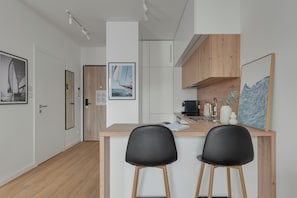 A modern kitchen with a wooden countertop, two black chairs, and a coffee machine. - Porto Regatta with Parking and Gym (Gdańsk)