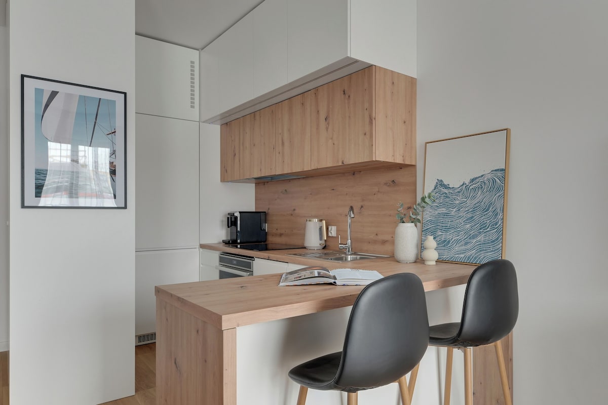 A modern kitchen with wooden cabinets, a built-in stove, and a bar area with two black chairs.