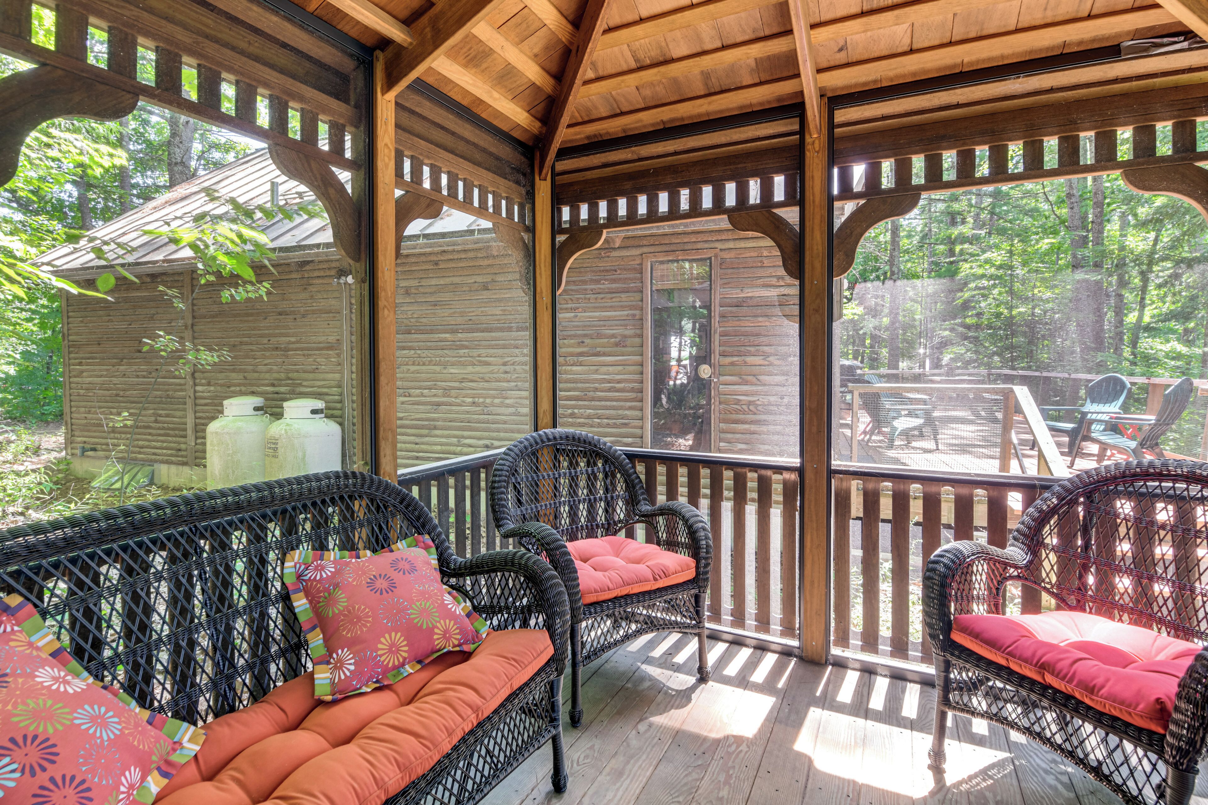 Un espace extérieur aménagé, abrité et doté de mobilier en osier et de coussins, offrant une vue sur un jardin et une structure en bois.