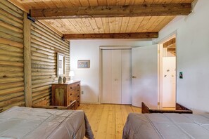 Ein Zimmer mit Holzwänden und schrägem Dach, ausgestattet mit zwei Betten, einem Schminktisch und einer Tür zu einem anderen Raum.