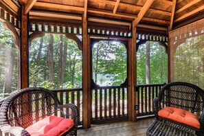 Eine Holzterrasse mit Korbstühlen und Blick auf einen Wald.