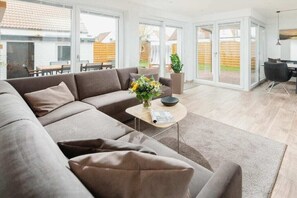 Ein modernes Wohnzimmer mit einem Ecksofa, einem Couchtisch mit Blumenvase und Blick ins Freie durch große Glasüren.