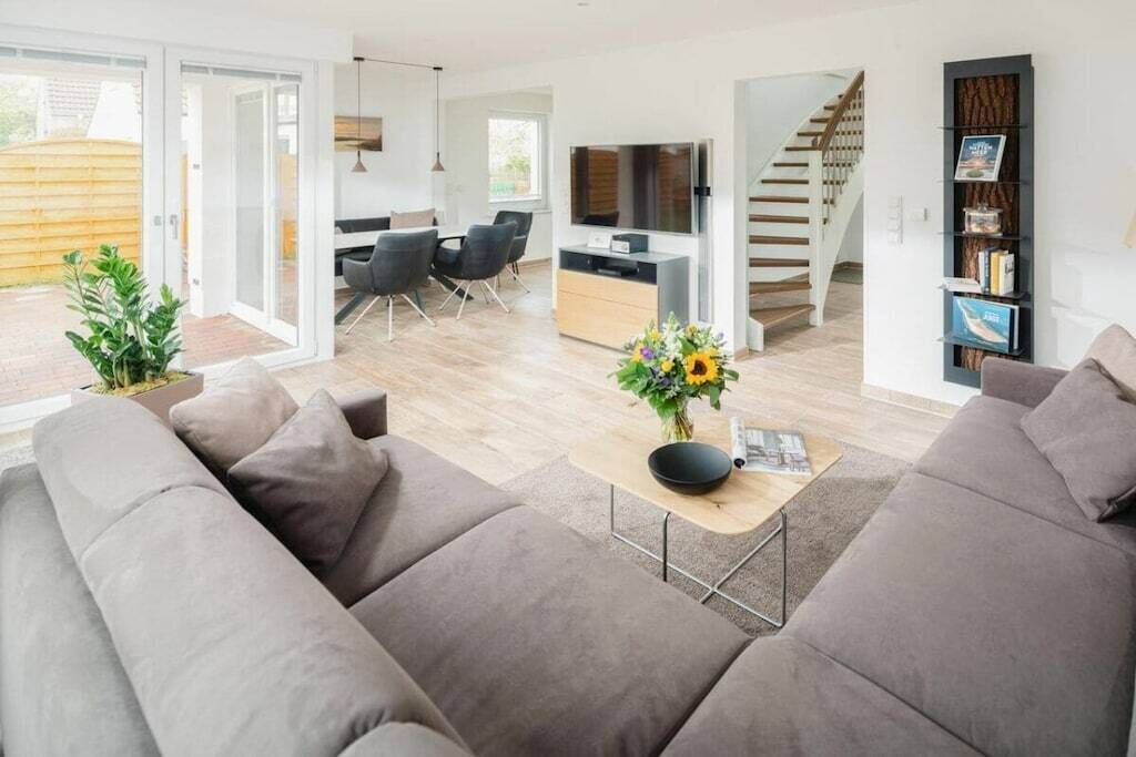 A modern living room with a sofa, a coffee table with a vase, and a staircase leading to another level.
