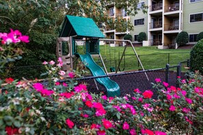 A playground with a green slide and a small shelter, surrounded by a fence and blooming flowers. - Pigeon Forge | Romantic Mountain Retreat | Trails + Attractions (Pigeon Forge)