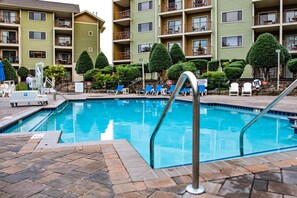 A swimming pool with lounge chairs and a poolside area, surrounded by apartment buildings with balconies and greenery. - Pigeon Forge | Romantic Mountain Retreat | Trails + Attractions (Pigeon Forge)