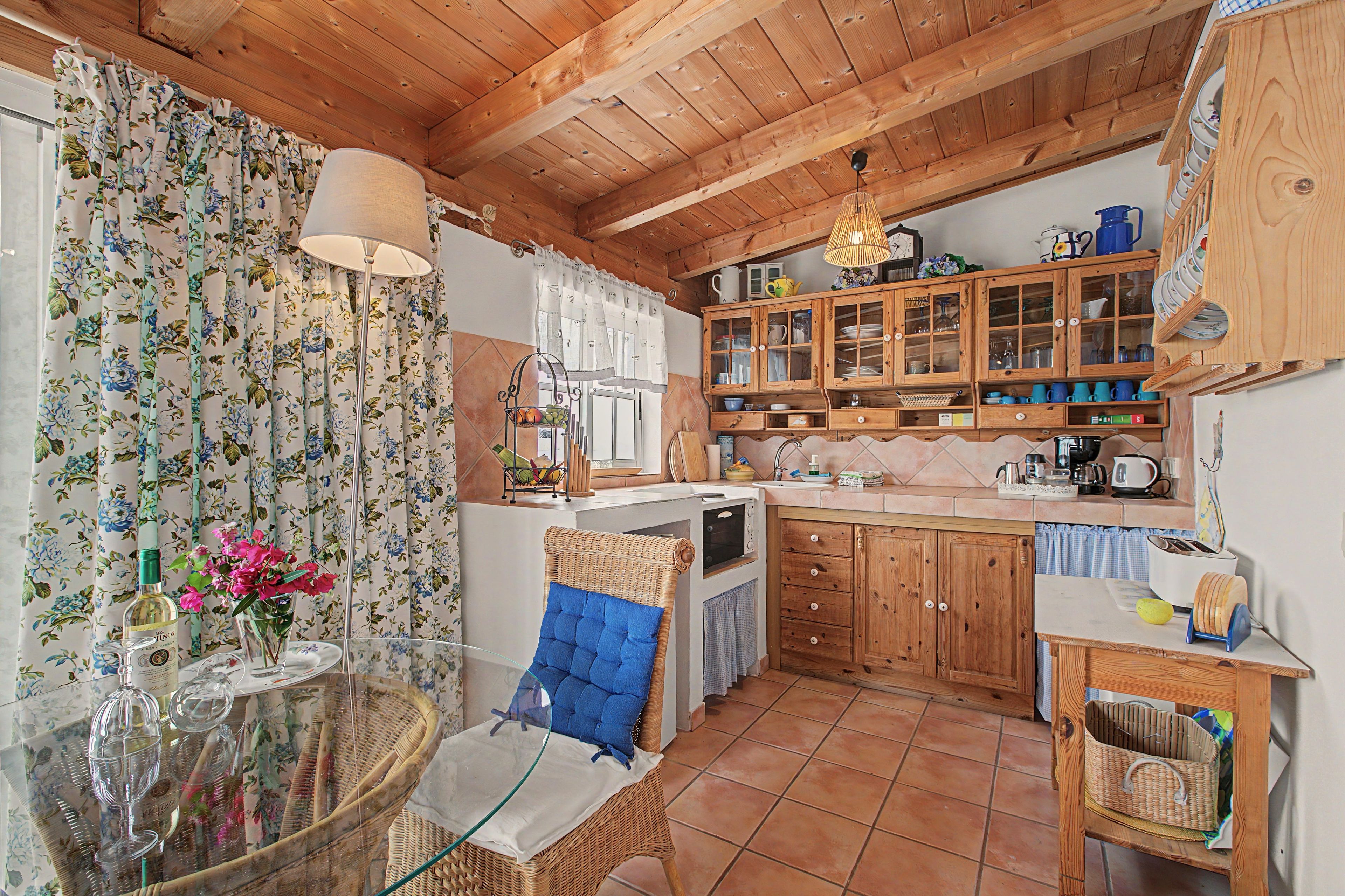 Una cocina rústica con armarios de madera, una mesa de comedor con sillas y una lámpara colgante.